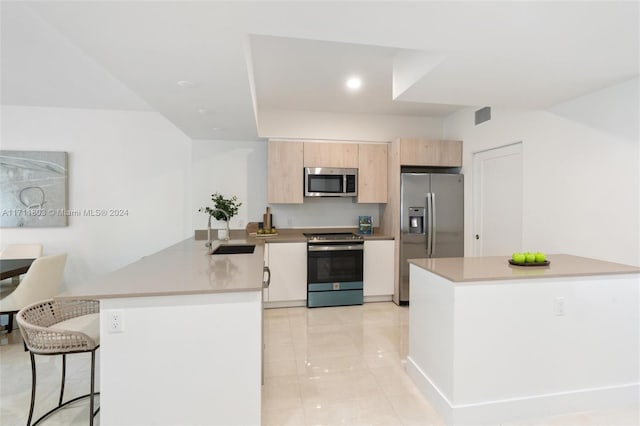 kitchen with kitchen peninsula, appliances with stainless steel finishes, sink, light brown cabinets, and a breakfast bar area