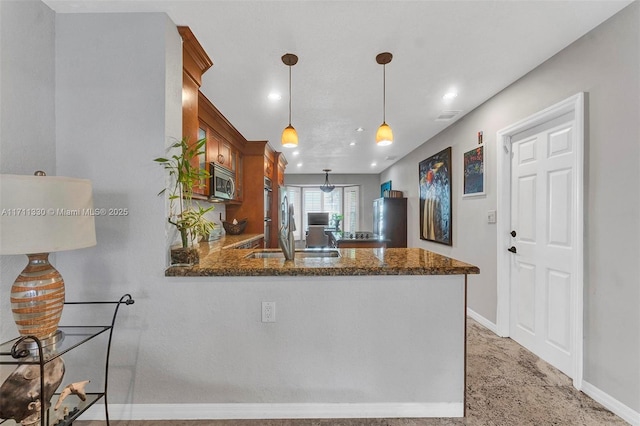 kitchen featuring sink, decorative light fixtures, kitchen peninsula, and dark stone counters