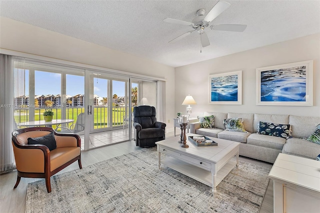 living room with ceiling fan, light hardwood / wood-style floors, and a textured ceiling