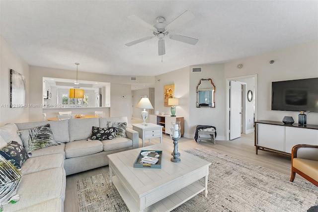 living room featuring a textured ceiling, light wood-type flooring, and ceiling fan