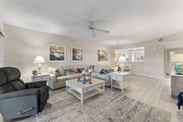 living room with ceiling fan, light hardwood / wood-style floors, and a textured ceiling