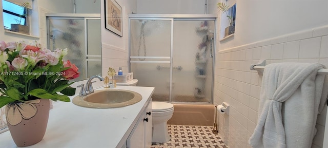 full bathroom with vanity, combined bath / shower with glass door, tile walls, and toilet