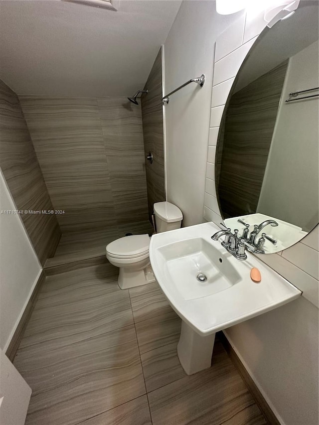 bathroom featuring a tile shower, toilet, tile patterned floors, and sink