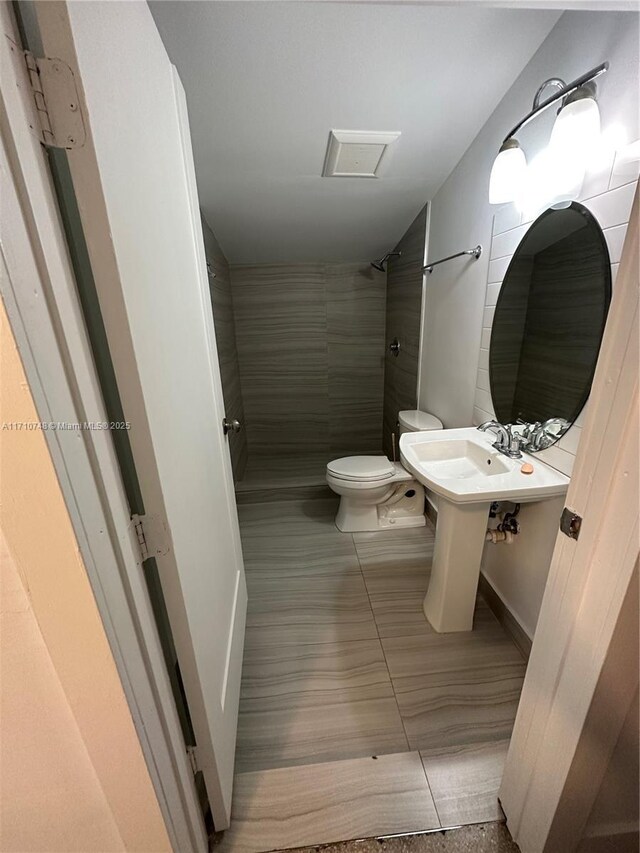 bathroom with tile patterned flooring, tiled shower, and toilet