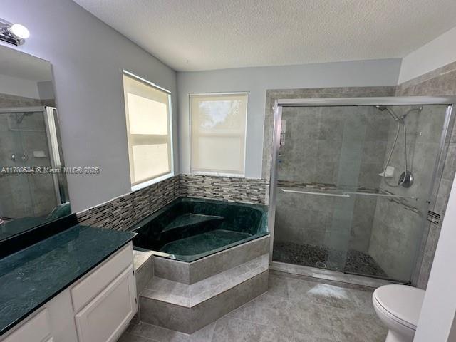 full bathroom with a textured ceiling, toilet, vanity, and separate shower and tub