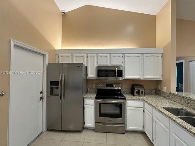 kitchen with light tile patterned floors, kitchen peninsula, stainless steel appliances, white cabinets, and light stone counters