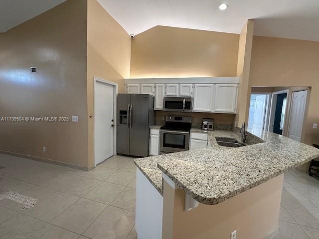 kitchen with kitchen peninsula, light tile patterned floors, stainless steel appliances, white cabinets, and light stone counters