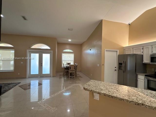 kitchen with white cabinetry, stainless steel appliances, light tile patterned floors, french doors, and light stone counters