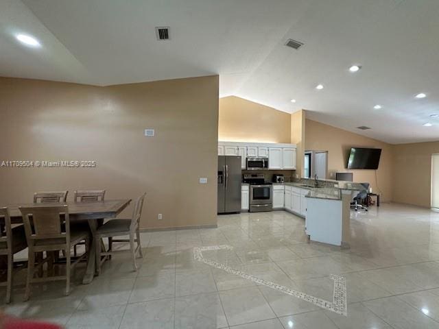 kitchen featuring lofted ceiling, kitchen peninsula, light stone countertops, stainless steel appliances, and white cabinets