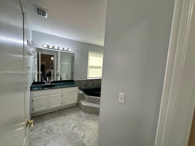 bathroom with a textured ceiling, a tub, and vanity