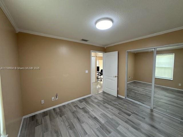 unfurnished bedroom with light wood-type flooring, a closet, crown molding, and a textured ceiling