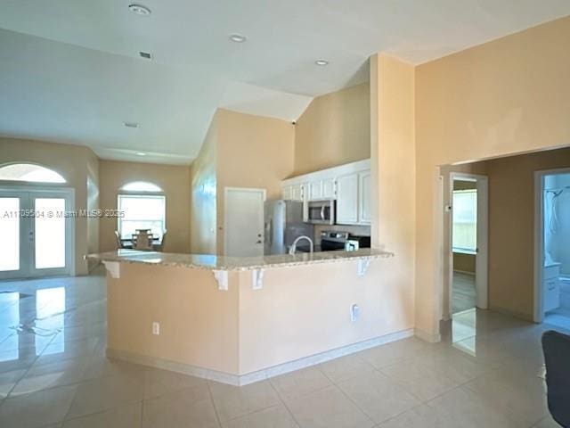 kitchen with light tile patterned floors, a kitchen bar, kitchen peninsula, appliances with stainless steel finishes, and white cabinets