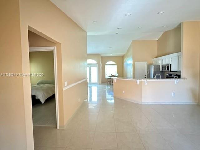 kitchen featuring white cabinets, appliances with stainless steel finishes, a kitchen bar, kitchen peninsula, and light tile patterned floors