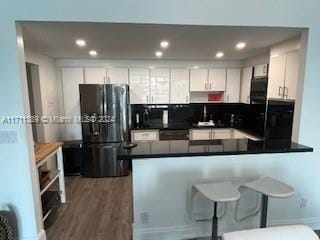 kitchen featuring stainless steel refrigerator, white cabinetry, dark hardwood / wood-style flooring, kitchen peninsula, and a kitchen bar