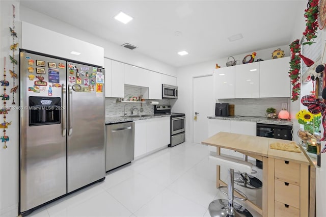 kitchen featuring light stone countertops, appliances with stainless steel finishes, tasteful backsplash, light tile patterned flooring, and white cabinetry