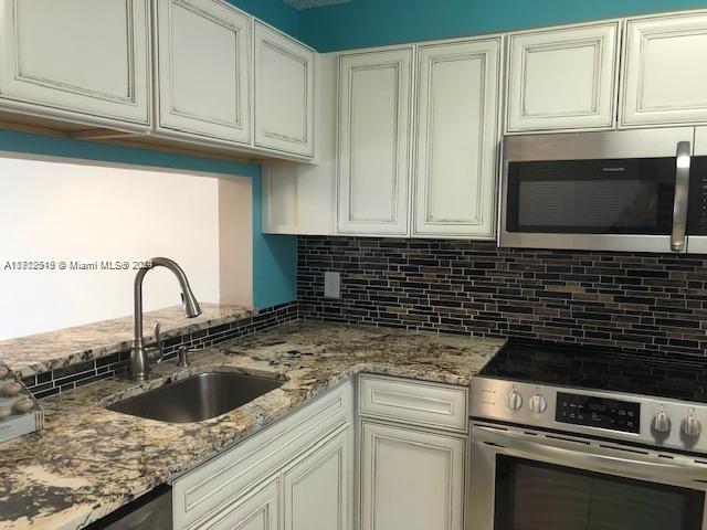 kitchen featuring sink, tasteful backsplash, light stone counters, white cabinetry, and stainless steel appliances