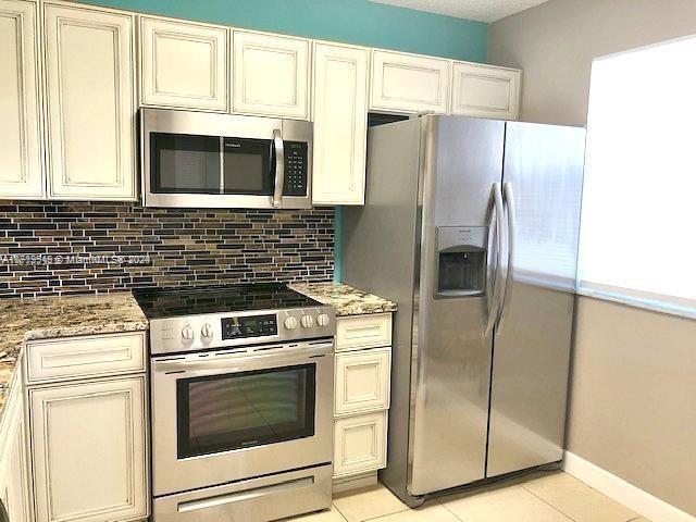 kitchen with light tile patterned floors, tasteful backsplash, cream cabinetry, light stone counters, and stainless steel appliances