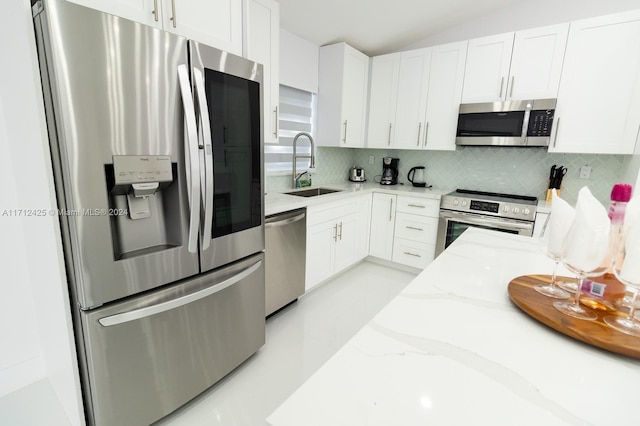 kitchen featuring tasteful backsplash, light stone counters, stainless steel appliances, sink, and white cabinetry