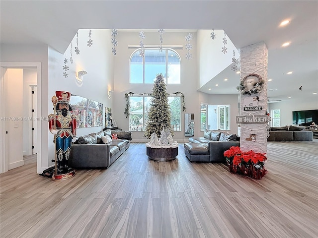 living room featuring a wealth of natural light, a towering ceiling, and light hardwood / wood-style floors