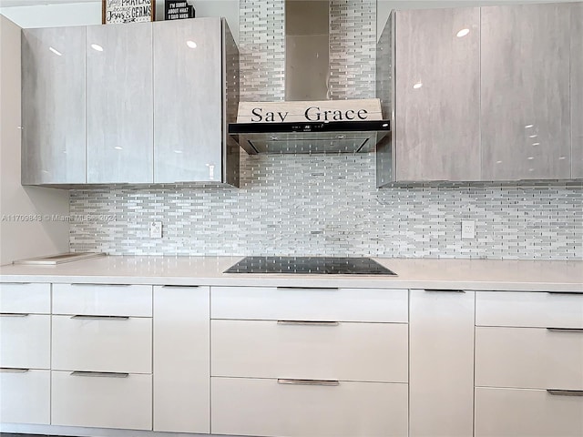 kitchen featuring decorative backsplash, black electric stovetop, white cabinets, and wall chimney range hood