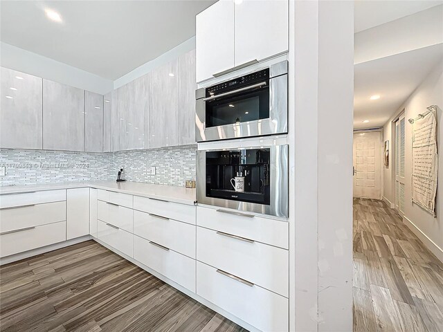 kitchen featuring white cabinets, light wood-type flooring, tasteful backsplash, and double oven