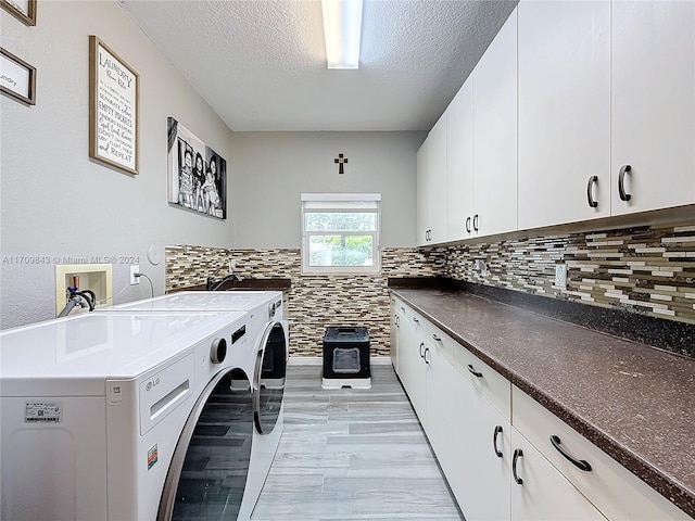 laundry room with cabinets, a textured ceiling, washing machine and dryer, and light hardwood / wood-style flooring