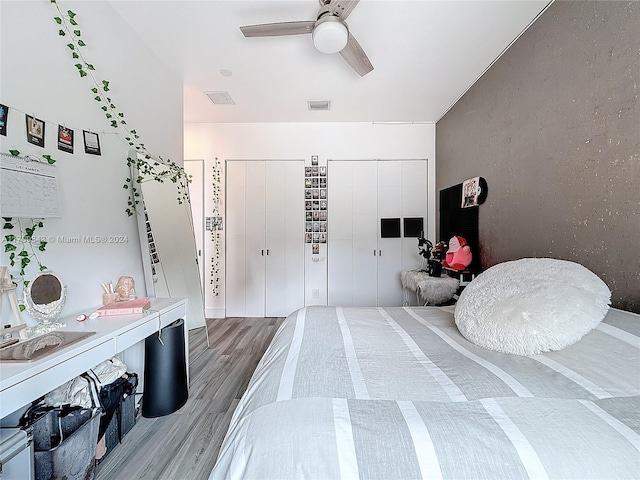 bedroom featuring ceiling fan, wood-type flooring, and two closets