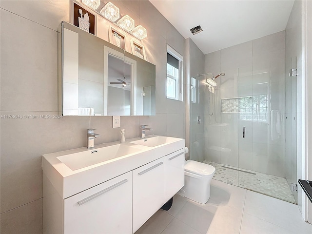 bathroom featuring ceiling fan, tile patterned flooring, toilet, a shower with shower door, and tile walls