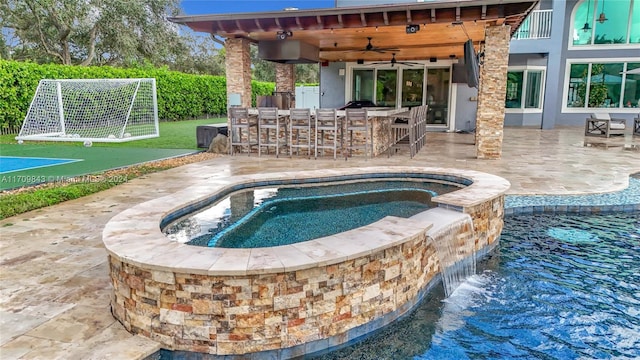 view of swimming pool featuring an in ground hot tub, ceiling fan, exterior kitchen, a bar, and a patio area