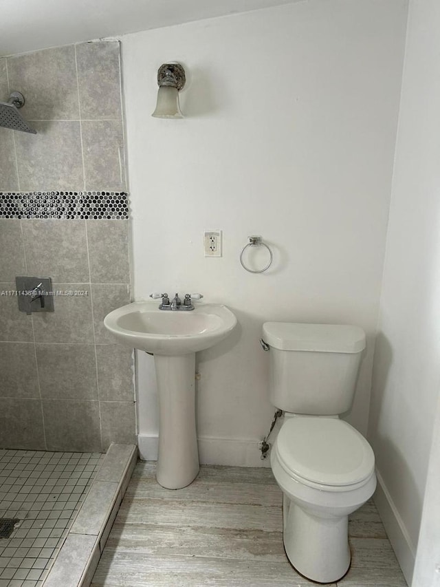 bathroom featuring a tile shower, sink, wood-type flooring, and toilet