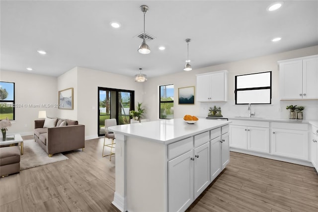 kitchen with sink, a center island, decorative light fixtures, white cabinets, and light wood-type flooring