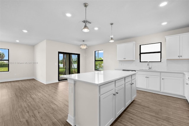 kitchen with white cabinets, decorative light fixtures, a kitchen island, and light hardwood / wood-style floors