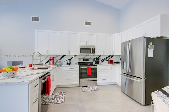 kitchen with a high ceiling, white cabinets, sink, appliances with stainless steel finishes, and light stone counters