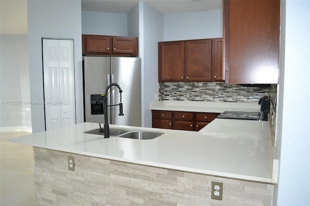 kitchen featuring stove, sink, stainless steel fridge, tasteful backsplash, and kitchen peninsula