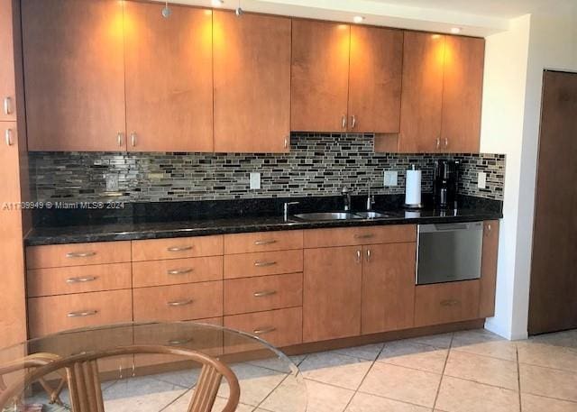 kitchen featuring tasteful backsplash, stainless steel dishwasher, sink, light tile patterned floors, and dark stone countertops