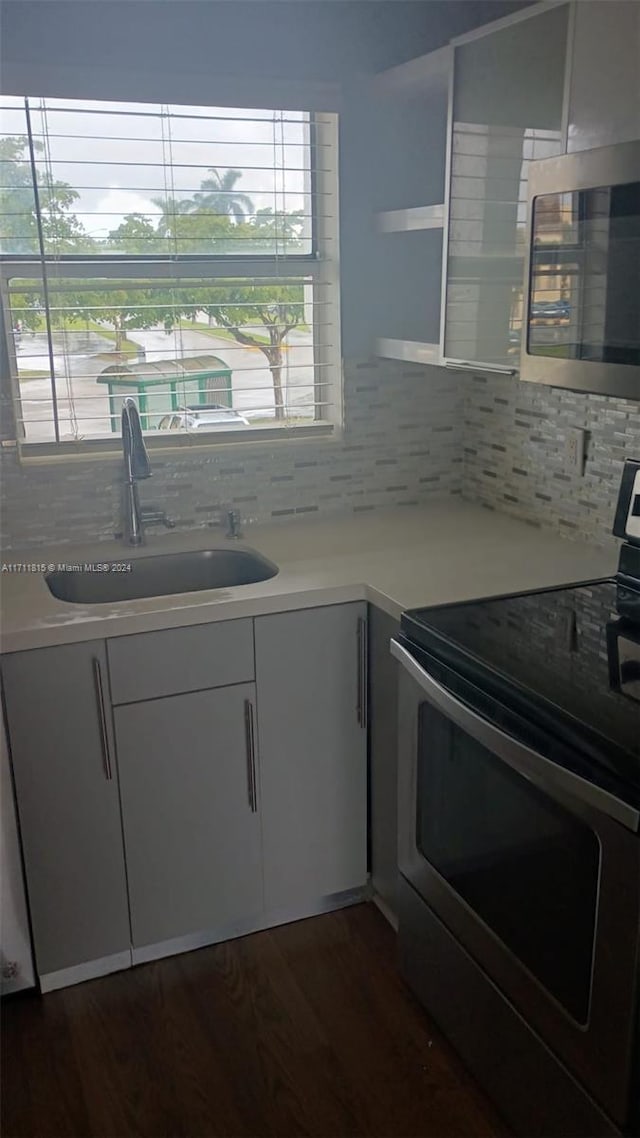 kitchen with appliances with stainless steel finishes, dark hardwood / wood-style flooring, backsplash, and sink