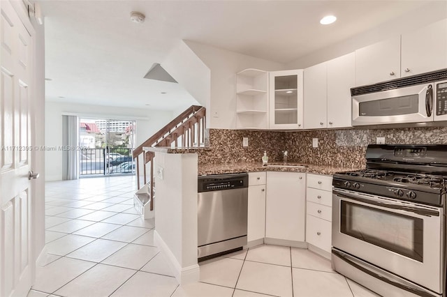 kitchen with white cabinetry, stainless steel appliances, tasteful backsplash, dark stone counters, and light tile patterned floors