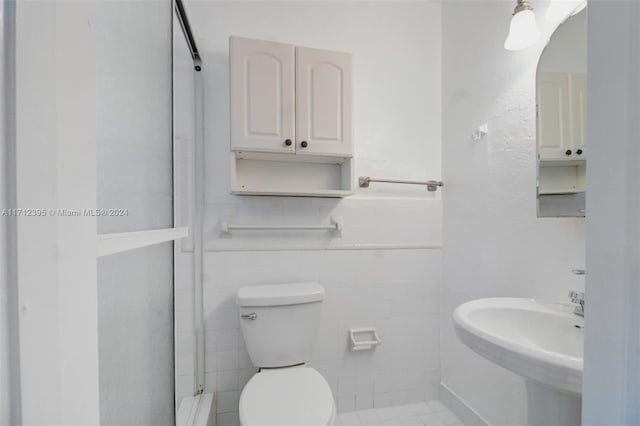 bathroom with sink, tile patterned flooring, a shower, toilet, and tile walls