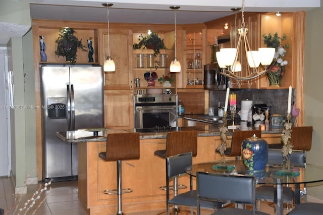 kitchen featuring appliances with stainless steel finishes, hanging light fixtures, light tile patterned floors, a breakfast bar, and decorative backsplash