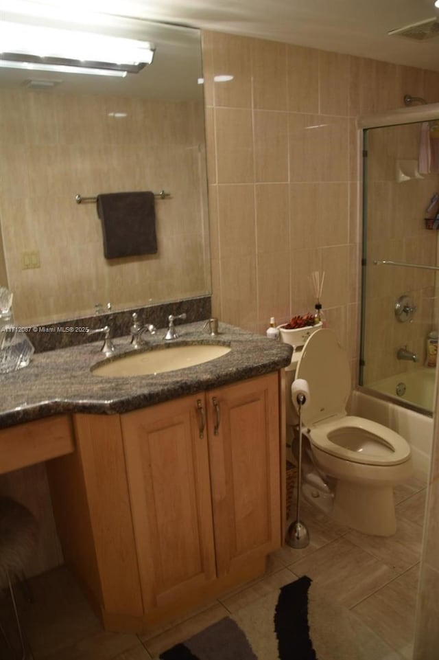 full bathroom featuring toilet, vanity, tile patterned floors, tile walls, and bath / shower combo with glass door