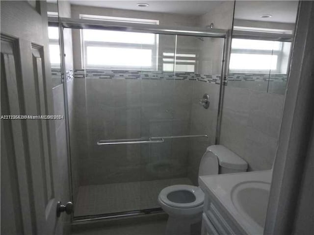 bathroom featuring a shower with door, vanity, a healthy amount of sunlight, and toilet