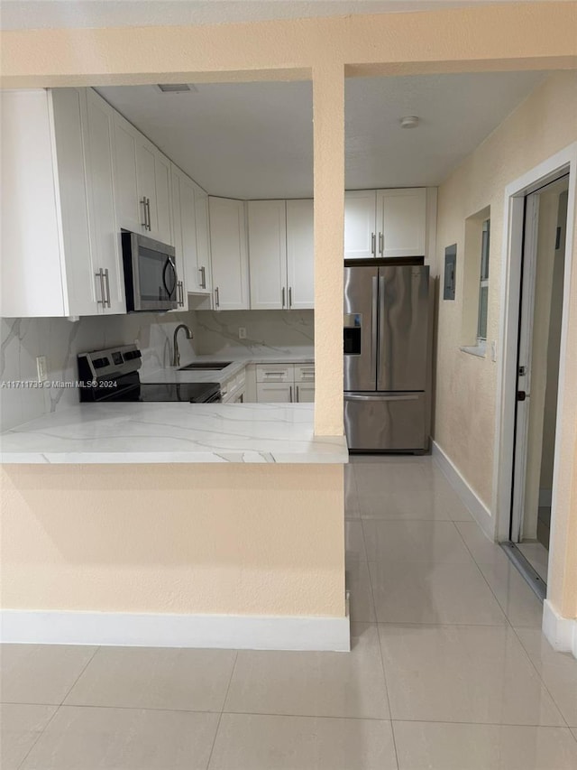 kitchen featuring sink, stainless steel appliances, light tile patterned floors, kitchen peninsula, and white cabinets