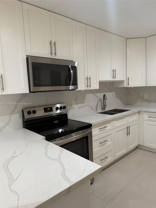 kitchen with stainless steel appliances, light stone counters, white cabinetry, and sink