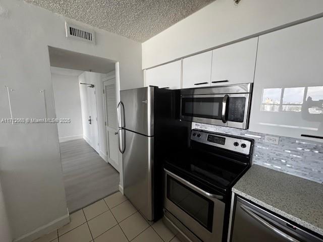 kitchen with light tile patterned floors, appliances with stainless steel finishes, white cabinets, visible vents, and a textured ceiling