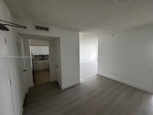 hallway featuring baseboards, visible vents, wood finished floors, and a textured ceiling