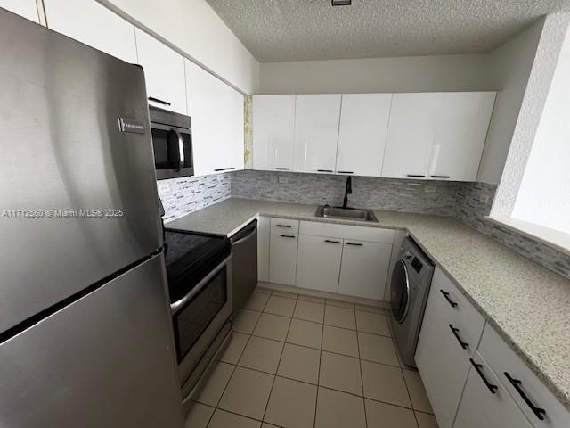 kitchen featuring tasteful backsplash, light tile patterned floors, appliances with stainless steel finishes, washer / dryer, and a sink