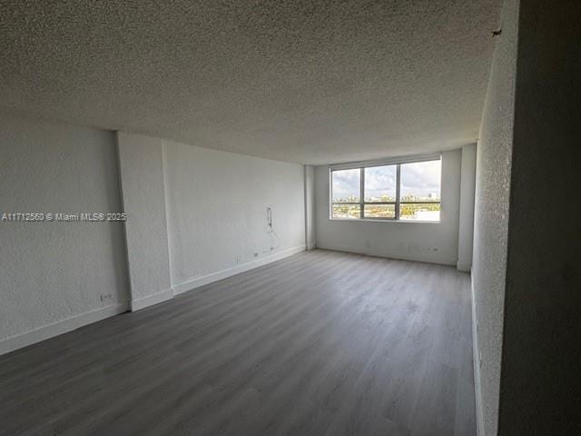 unfurnished room featuring a textured ceiling, a textured wall, wood finished floors, and baseboards