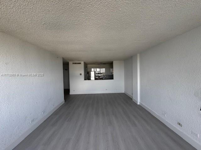 empty room featuring dark wood-style flooring, baseboards, and a textured ceiling