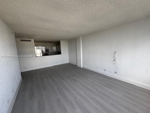 unfurnished living room featuring dark wood-type flooring, visible vents, baseboards, and a textured ceiling
