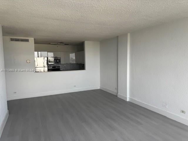 unfurnished living room with a textured ceiling, dark wood-style flooring, baseboards, and visible vents